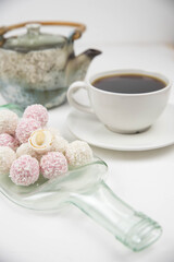 White coconut candy balls on handmade upcycle plate from the bottle. Coconut cookies on white background with the cup of tea. Teapot with black tea. 
