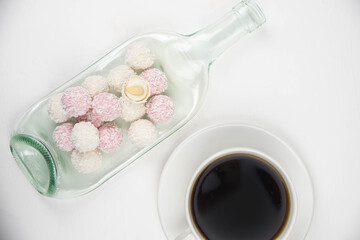 White coconut candy balls on handmade upcycle plate from the bottle. Coconut cookies on white background with the cup of tea. Teapot with black tea. 