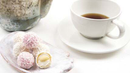 Obraz na płótnie Canvas White coconut candy balls on handmade plate. Coconut cookies on white background with the cup of tea. Teapot with black tea. 