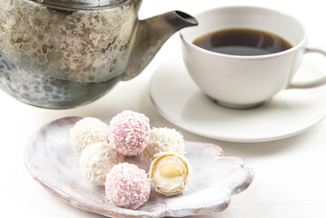 White coconut candy balls on handmade plate. Coconut cookies on white background with the cup of tea. Teapot with black tea. 