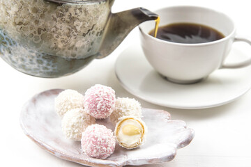White coconut candy balls on handmade plate. Coconut cookies on white background with the cup of tea. Teapot with black tea. 