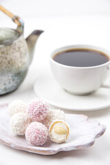 White coconut candy balls on handmade plate. Coconut cookies on white background with the cup of tea. Teapot with black tea. 