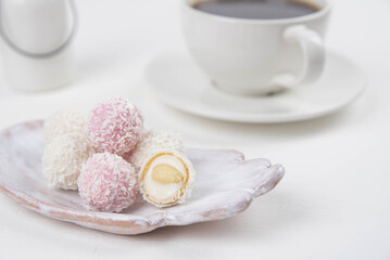 White coconut candy balls on handmade plate. Coconut cookies on white background with the cup of tea. Teapot with black tea. 