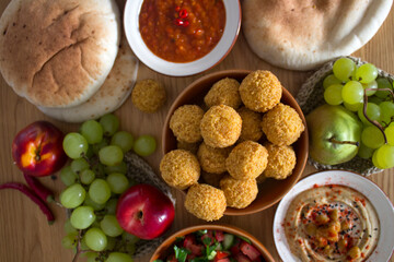   Authentic food of Middle East. Plate of hummus, falafels, pita bread, harissa sauce, tahini, fresh salad and fruits on wooden table. Traditional meals of Israel top view photo. Beautiful food pictur