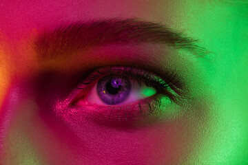 Eyes. Portrait of female fashion model in neon light on dark studio background. Beautiful caucasian...