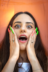 Shocked or surprised beautiful young woman with colored nails holding her cheeks  and shouting