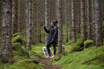 A young woman taking a cell phone photo along a trail in the woods