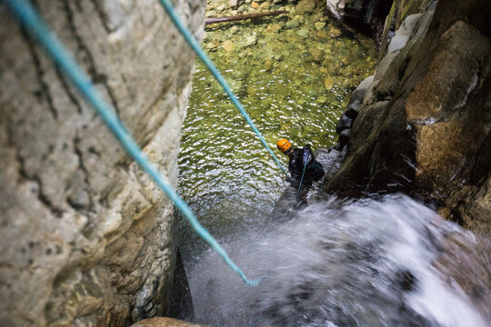 Man standing on ledge while rappelling down waterfall in canyon.