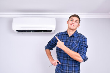 Joyful professional fixer installed indoor air conditioner, points finger and smiles, good service