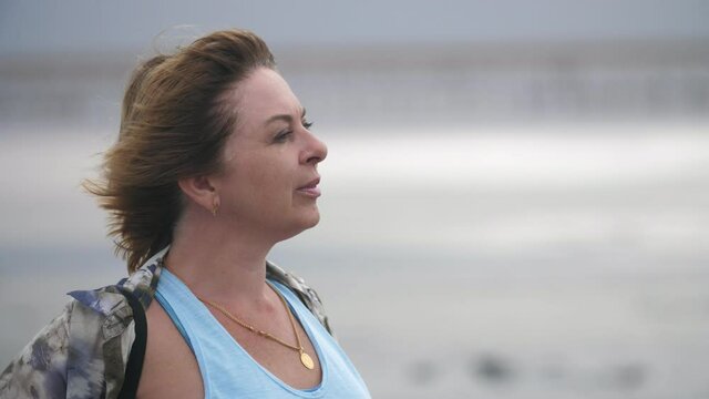 Enthusiastic woman standing on a sea beach in a windy weather in slow motion