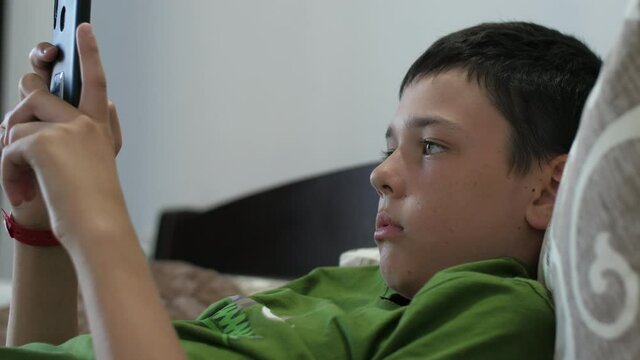 Relaxed boy lying and playing video games on his smartphote in an apartment