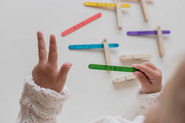 Child solves math examples with wooden sticks , didactic materials , Diy, home education. Mathematics for preschooler.