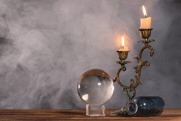 Crystal ball and burning candle on the table in the smoke.