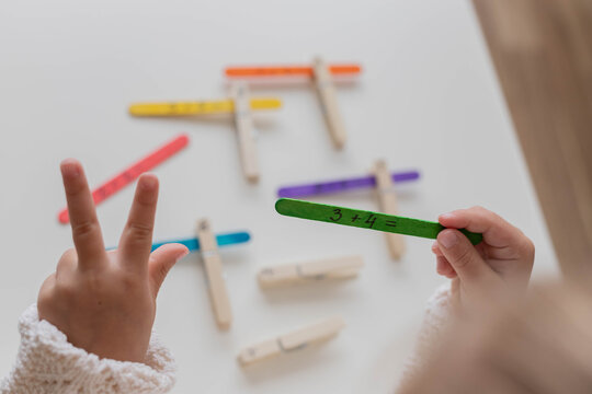Child solves math examples with wooden sticks , didactic materials , Diy, home education. Mathematics for preschooler. - Powered by Adobe