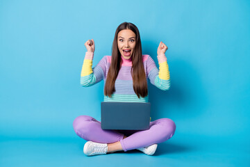 Portrait of pretty glad cheerful girl sitting lotus position crossed legs using laptop having fun isolated over bright blue color background