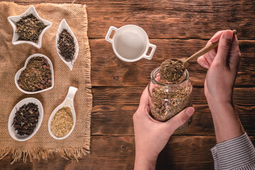 Woman is sorting a dried tea leaves into a bowl on brown wooden table background.