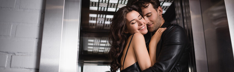 Happy young adult couple with closed eyes embracing each other at elevator entrance, banner