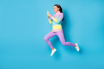 Fototapeta na wymiar Full length body size view of nice addicted focused cheerful girl jumping using gadget 5g free time isolated on bright blue color background
