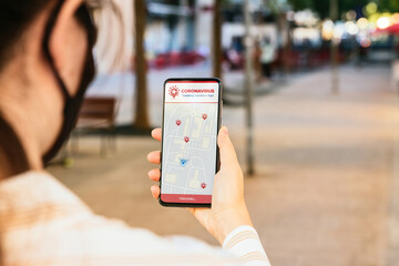 Stock photo of a young woman using a Coronavirus tracking app in her phone. The locations of infected people appear on the screen