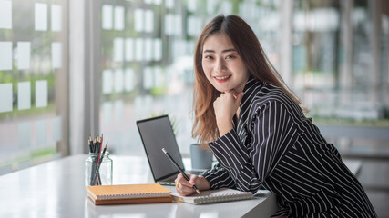 Young asian businesswoman working on laptop and taking note while sitting at the table in office.