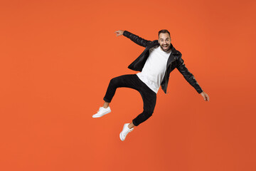 Fototapeta na wymiar Full length of excited cheerful young bearded man 20s in basic white t-shirt black leather jacket jumping spreading hands looking camera isolated on bright orange colour background studio portrait.
