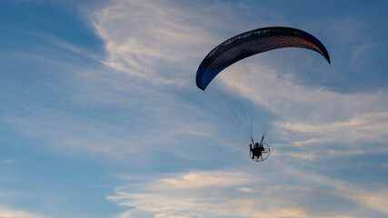 Silhouette of powered paraglider against the blue sky