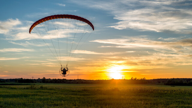 Beautiful landscape with back view of paramotor pilot during sunset