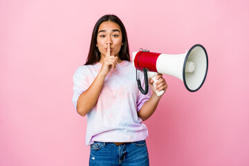 Young asian woman holding a megaphone isolated on pink background keeping a secret or asking for...