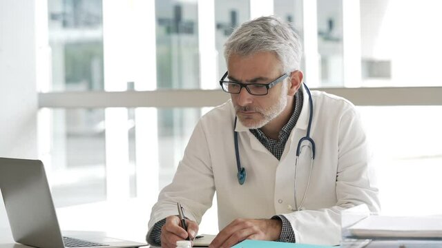 Doctor in office writing on agenda, sitting at desk