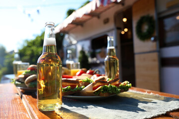 Bottles of beer and sandwiches on wooden table near motorhome. Camping season