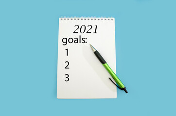 List of goals for the New Year 2021. White notepad and green pen isolated on blue background.