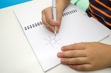 child's hand draws the sun on a white notepad.