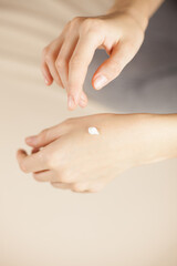 girl applies white cream on her hands on a beige background, taking care of herself and the skin. a drop of cream on the wrist