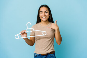 Young asian woman holding a hanger isolated on blue background showing a mobile phone call gesture with fingers.