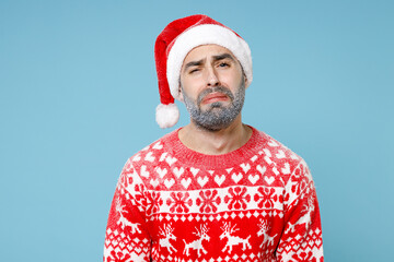 Upset crying Northern bearded man frozen icy snow face in Santa hat Christmas sweater looks camera isolated on blue background in studio. Happy New Year celebration merry holiday winter time concept.