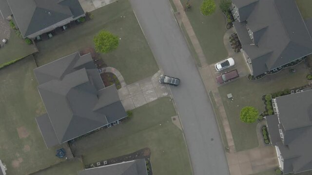 Drone follows and tracks a black car through a suburban neighborhood from a birds eye view during the day