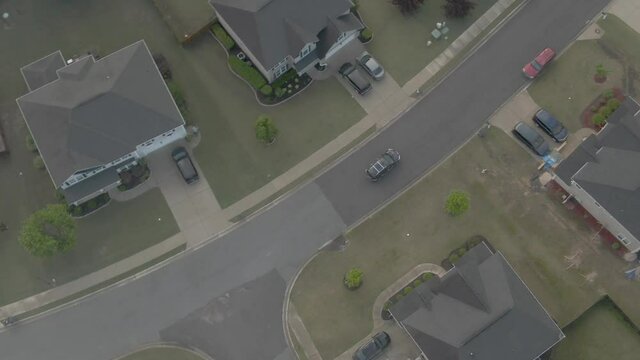 Drone follows a black car through the rest of the neighborhood as it passes house during the day