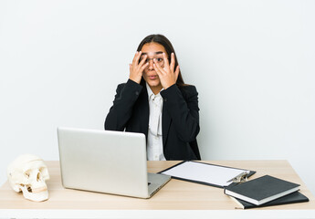 Young traumatologist asian woman isolated on white background blink through fingers frightened and nervous.