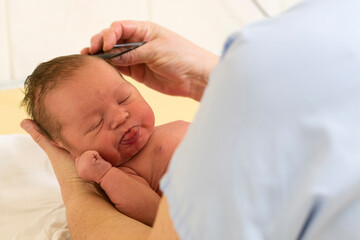 Woman combing a newborn with a comb and holding it in her hand.