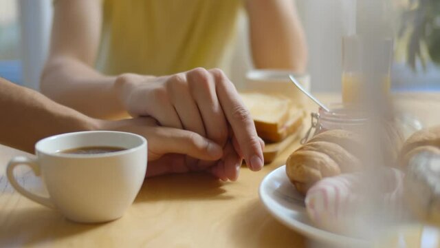 Young cheerful man holding gay partner hand having breakfast in morning