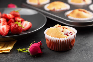 Strawberry muffins with fresh flowers on black concrete background