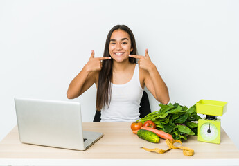 Young dietician asian woman isolated on white background smiles, pointing fingers at mouth.