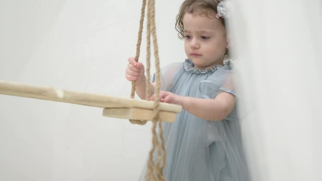 beautiful little girl in blue dress playing with wooden with rope swing seesaw during indoors leisure holiday activity