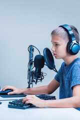 Portrait of teenage boy wearing headphones using computer keyboard and microphone. Online learning, remote education, video game, podcast concept