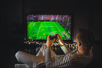 Young hipster man playing video game football soccer on console. gamer guy with gamepad controller...