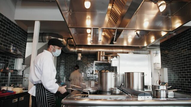 Chefs in protective masks and gloves prepare food in the kitchen of a restaurant or hotel, high kitchen during coronavirus covid 19 pandemic, business reopen after quarantine