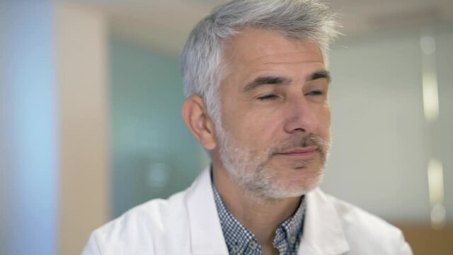 Portrait of confident doctor with grey hair standing in hospital hallway