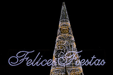 Christmas tree illuminated next to the text Happy Holidays written in Spanish © juanorihuela