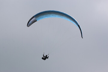 Paraglider flying blue wing in a cloudy sky
