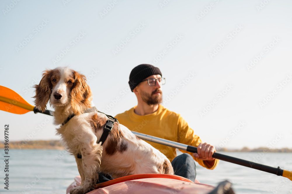 Wall mural man with a dog in a canoe on the lake. young male person with spaniel in a kayak row boat, active fr